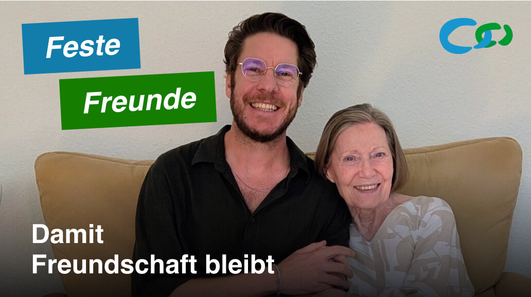 Marion und Philipp, ein Besuchspaar, sitzen lachend auf dem Sofa